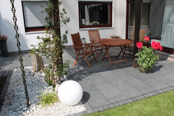 Gepflasterte Terrasse aus Granitplatten mit Holzmöbeln und Kugelleuchte